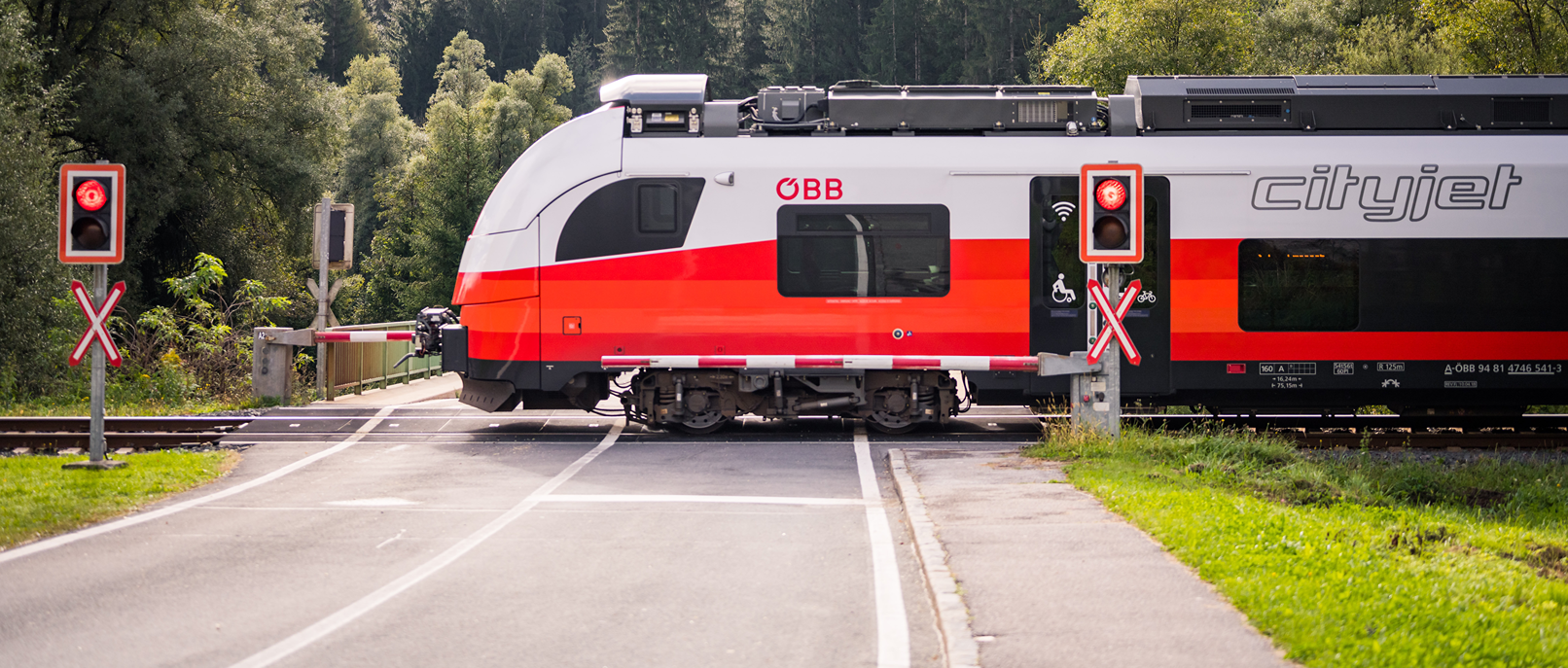 Vlak Cityjet ÖBB na Koroškem vozi čez nivojski prehod.